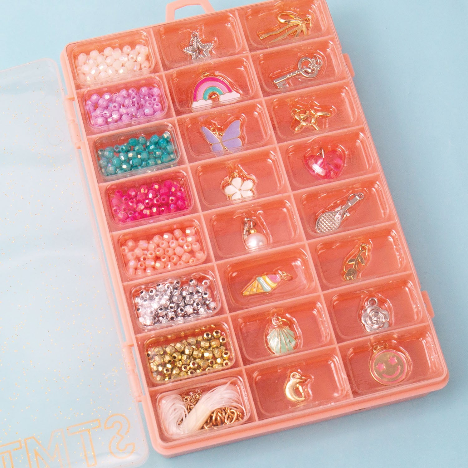Pink jewelry organizer with compartments filled with beads and charms on a light blue background.