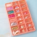 Pink jewelry organizer with compartments filled with beads and charms on a light blue background.