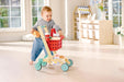 Child playing with a wooden toy shopping cart in a bright room.