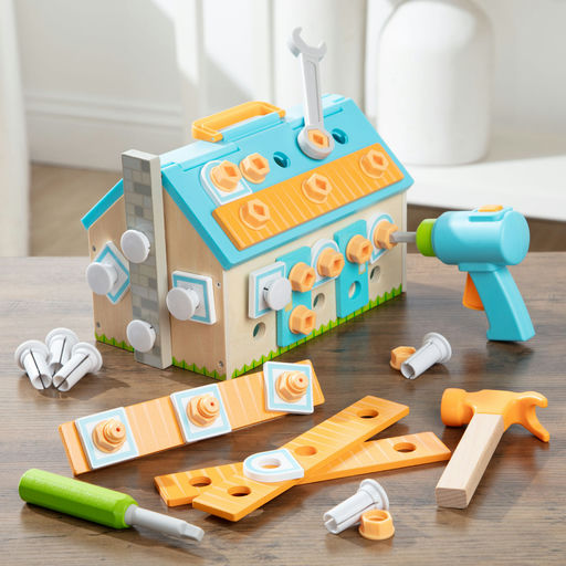 A children's wooden toy house construction set on a tabletop, featuring a house-shaped building with orange and blue panels, loose screws, bolts, a green screwdriver, orange and beige wooden pieces, and a turquoise toy drill. No people or animals are present.