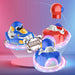 Three small toy spacecraft or ride-on vehicles shown in a stylized studio render: one blue with a cartoon duck face, one red with a helmet-like top, and one blue viewed from the back with glowing pink light effects. The scene has a pink-to-blue gradient background and comic-style 'BOOM' clouds.