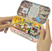 A person's hands holding open a small metal tin-shaped craft box labeled 'Dream Market' and 'Halloween Fair.' The inside features colorful miniature market stalls, tiny figures, a printed story panel on the lid, and warm LED lighting.