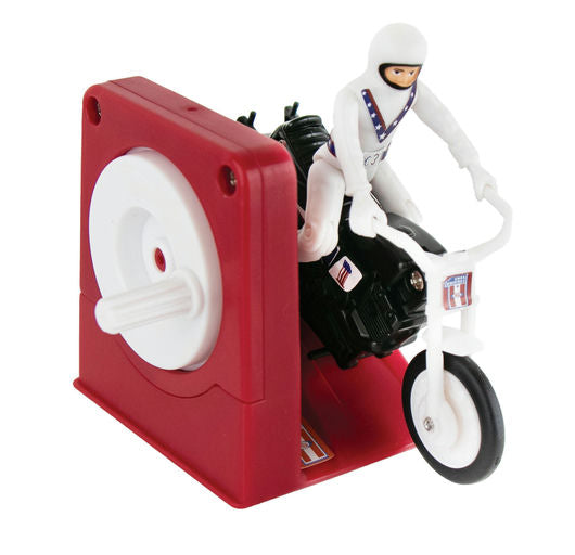 A vintage toy motorcycle with a white racer figure mounted on it, set against a red plastic crank mechanism on a plain white background.