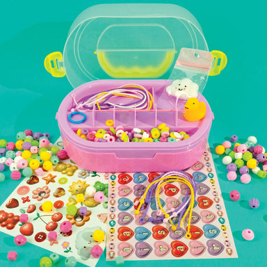 A colorful bead and craft kit with a pink plastic organizer case, yellow lid, and assorted beads, cords, and decorative pieces arranged on a bright teal background.
