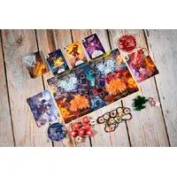 A card deck and matching cards arranged on a light wood plank surface, with a small box, a gold coin, and a few colorful decorative items around it.