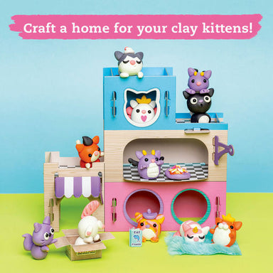 A colorful clay-kitten playset shown on a bright blue and green background with a pink banner reading 'Craft a home for your clay kittens!'. The set includes a multi-level house with blue, beige, and pink sections, several small animal figures, a small market stall, and accessories.
