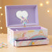 A pastel unicorn-themed music box jewelry box with an open lid showing a white unicorn figure on a stand and a heart-shaped mirror inside. The box has a lavender interior and exterior with pink, blue, and yellow unicorn and rainbow illustrations, plus a drawer front.