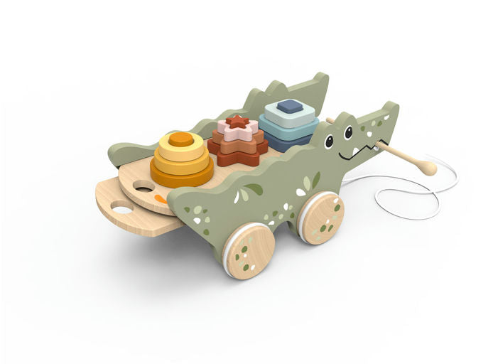 A wooden toy dinosaur cart with a smiling face, green body, natural wood wheels, and a string handle, carrying colorful stacking and sorting blocks on a white background.