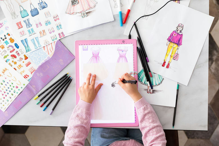 Child drawing on a tablet with fashion illustrations around