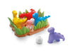 A colorful children's toy set featuring dinosaur figures and egg-shaped pieces on a base with grass, shown on a clean white background. The set includes yellow, red, blue, pink, purple, white, green, and brown pieces.
