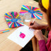 Person drawing with watercolor pencils on a wooden table with a colorful pencil set and water glass.